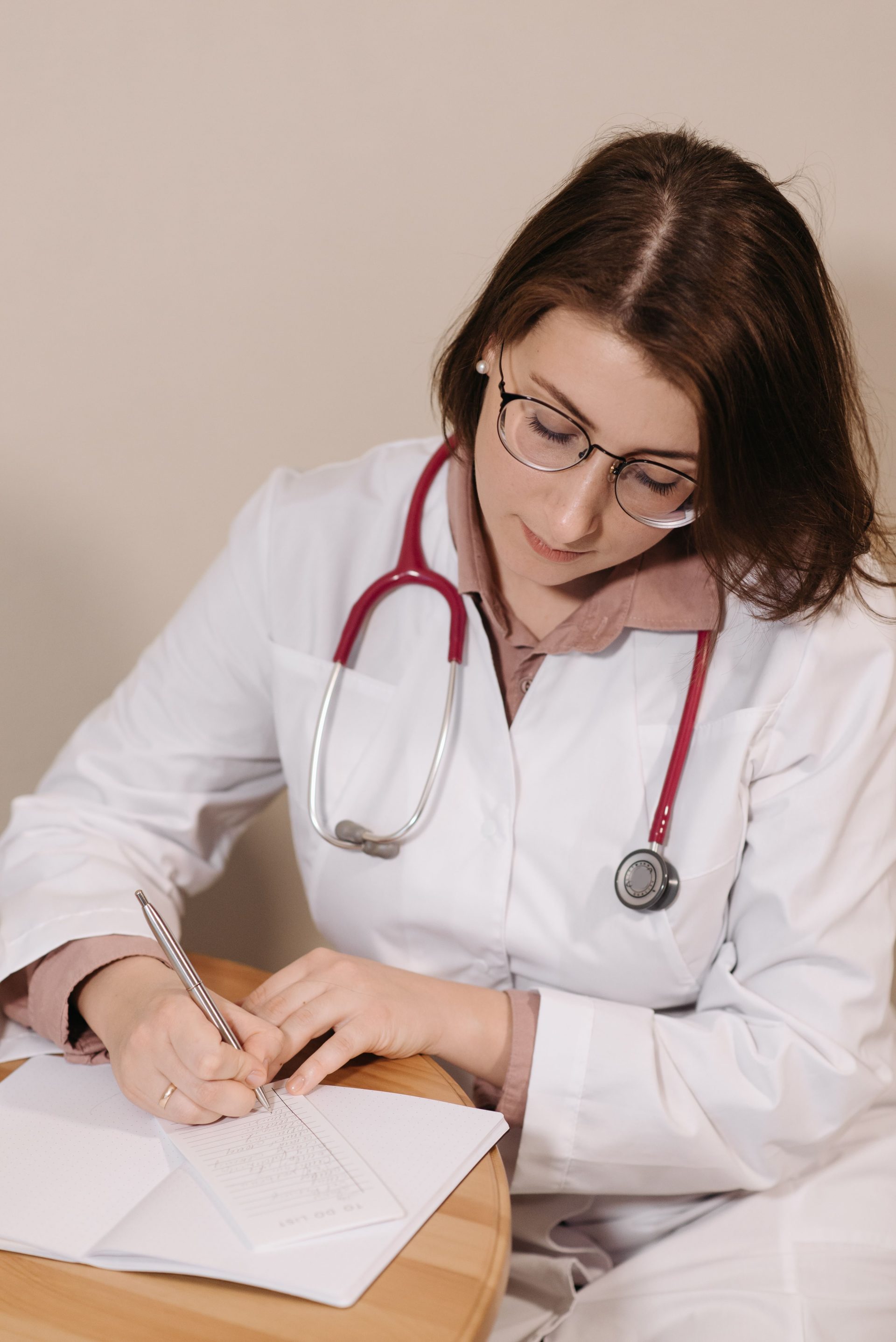 Female doctor writing a prescription in a clinical setting. Professional medical attire with stethoscope.